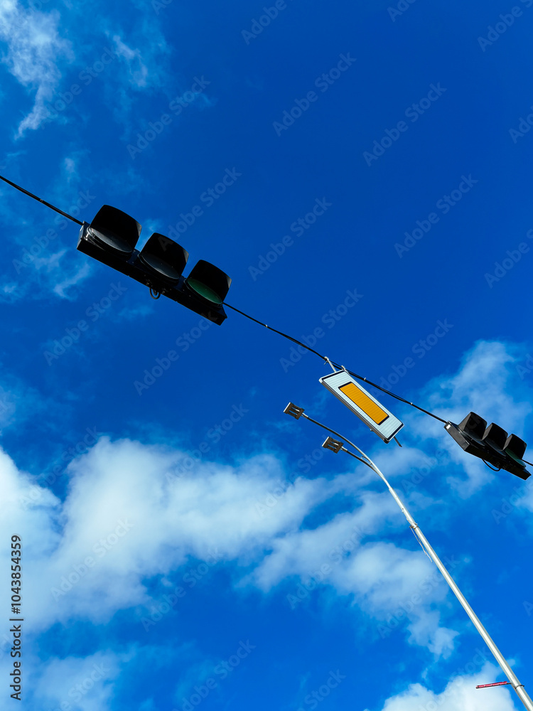 Urban traffic lights against a clear blue sky with scattered clouds, symbolizing transportation and city life. Vertical photo
