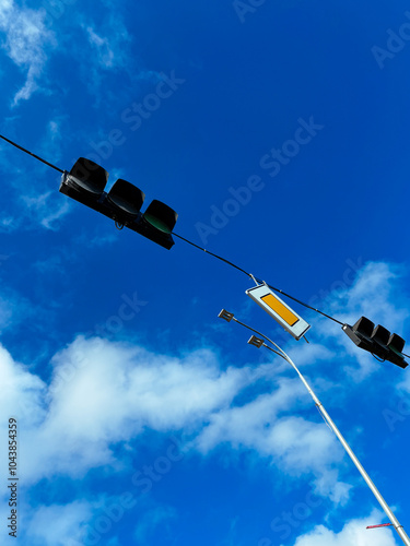 Obraz na płótnie Urban traffic lights against a clear blue sky with scattered clouds, symbolizing transportation and city life. Vertical photo w salonie