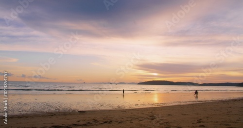 Serene Sunset Over Tranquil Beach with Silhouetted Figures Strolling Along the Shoreline Under a Sky Reflecting on Calm Ocean Waters, accentuating the tranquil environment and peaceful ambiance