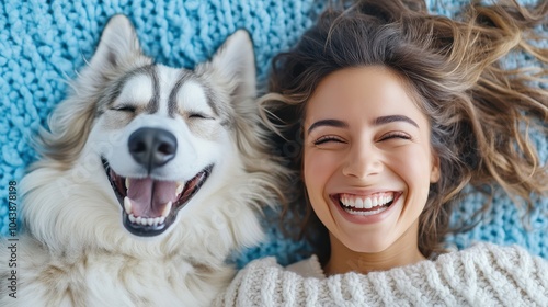 A joyful woman lies next to her fluffy husky on a textured blue mat, both sharing a hearty laugh, symbolizing friendship, joy, and carefree moments.