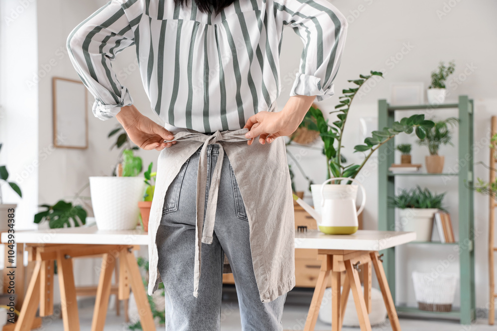 Young woman tying apron while preparing to take care of houseplants at home, back view Young woman tying apron while preparing to take care of houseplants at home, back view