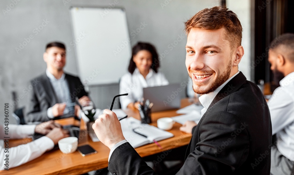 Business Career. Young Businessman At Corporate Meeting With Colleagues Smiling To Camera Sitting In Modern Office. Business Career. Young Businessman At Corporate Meeting With Colleagues Smiling To Camera Sitting In Modern Office.