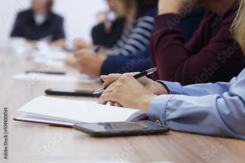 A woman with a pen sits next to her colleagues and prepares to write down information in a notebook. Meeting, seminar or training. Exam or colloquium. Photo. Faceless