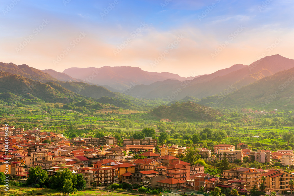 Obraz premium wonderful landscape of sunset valley town with beautiful fields, gardens, green plantations among great mountains and scenic evening cloudy sky on background of landscape