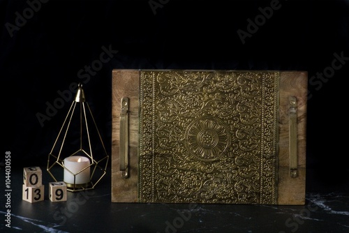 A brown box with gold engraved floral patterns on a black surface with a lit candle beside it. photo