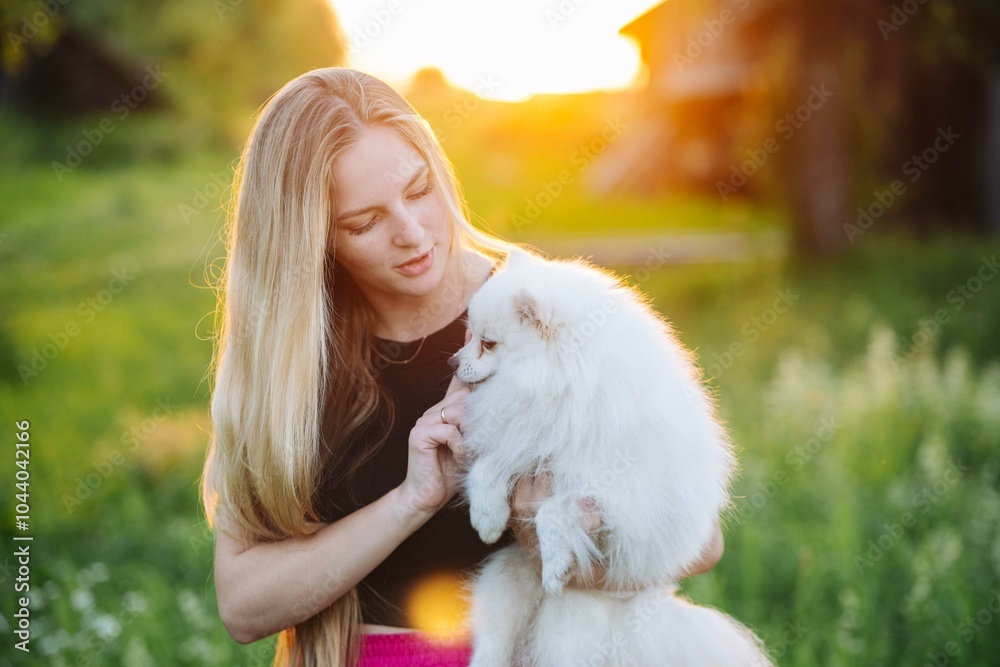 Blonde woman lovingly caresses her fluffy white dog in a lush field at sunset, radiating love and happiness in nature Blonde woman lovingly caresses her fluffy white dog in a lush field at sunset, radiating love and happiness in nature