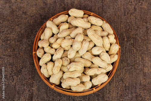 Unpeeled peanuts in a container isolated on a dark background. close up of salted shell peanuts.