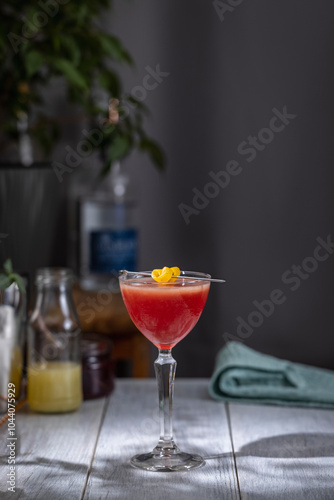 Red cocktail standing on table with garnish and bottles in background