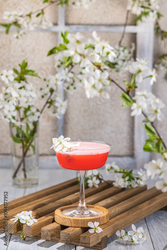 Refreshing pink cocktail standing on wooden table with spring flowers decoration