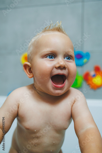 A baby boy is playing and smiling while sitting in a white bathtub with water. Bathing a baby.