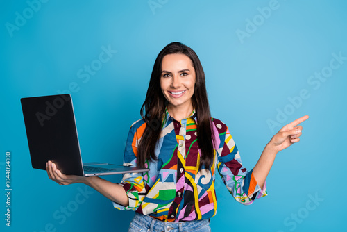 Portrait of positive girl with straight hair dressed blouse hold laptop indicating at sale empty space isolated on blue color background