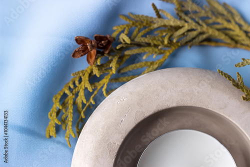 Round concrete candlestick of beige color on blue fabric among the branches of thuja. Shallow depth of field. Focus on the front of the candlestick.