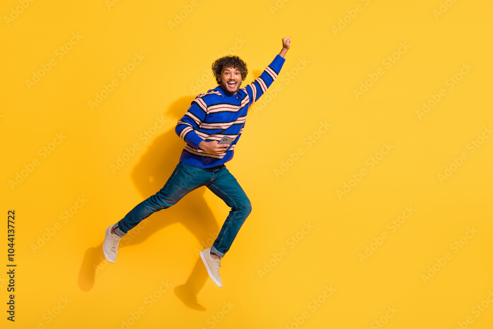 Full body photo of attractive young man hold device fly superman dressed stylish blue striped clothes isolated on yellow color background Full body photo of attractive young man hold device fly superman dressed stylish blue striped clothes isolated on yellow color background