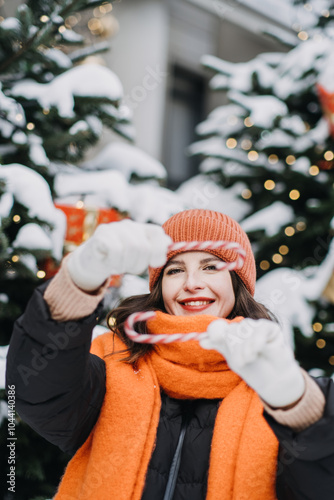 Smiling woman holding candy cane outdoors, dressed in winter attire, surrounded by snow-covered Christmas trees, holiday joy and festive spirit