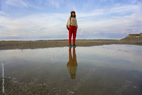 A person standing by a puddle, showing their reflection in the water. The image evokes themes of duality, self-reflection, and alternate perspectives.	