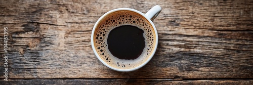 A bird's-eye view of a hot black coffee in a white cup placed atop a rustic wooden table surface. photo