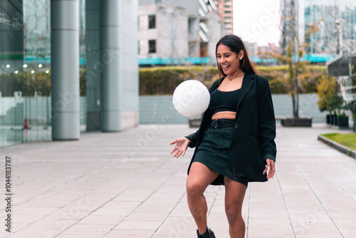 Beautiful brunette businesswoman holding and playing with soccer ball. Wearing office suit and skirt. Leaving work to train and play football. Outdoors. Sports and wellness advertising.