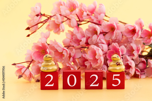 New year 2025 year of the Snake. Golden snake decorated with branch pink sakura flowers on yellow background.