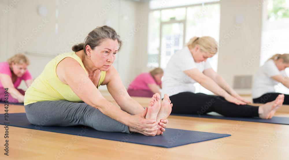 Obraz premium Active elderly woman practicing stretching yoga postures on mat at group class