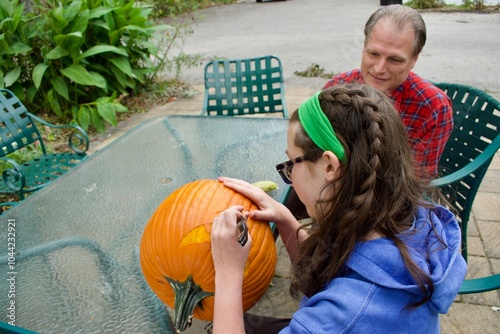 Teenage girl carving a pumpkin with her uncle watching