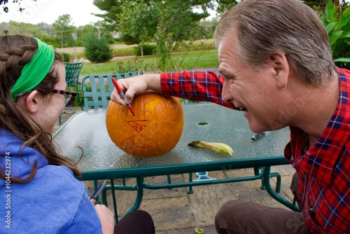 Laughing  man with teenage girl marking a pumpkin to carve