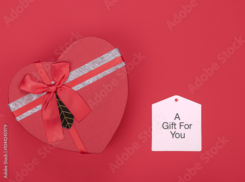 Heart shaped box with a red bow on a red background and a label photo