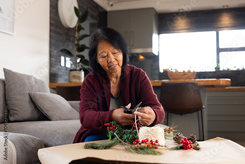 asian senior woman crafting Christmas decorations at home, enjoying festive preparations photo