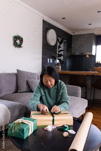 Elderly asian senior woman wrapping Christmas gifts at home, focusing on festive details photo