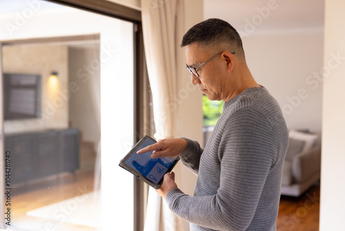 Asian senior man using tablet to control smart home system by window photo