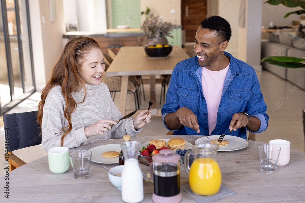 multiracial couple enjoying breakfast together at home, smiling and sharing pancakes multiracial couple enjoying breakfast together at home, smiling and sharing pancakes