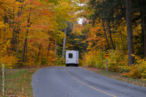 Camper van truck driving on a road surrounded by colorful maple trees with bright yellow leaves in fall season. Killbear Provincial Park, Ontario, Canada. photo