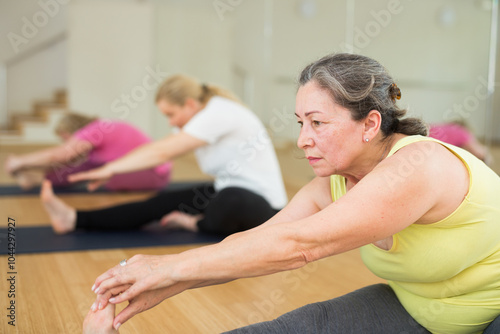 Three mature European women are doing head-to-knee pose in a fitness room photo