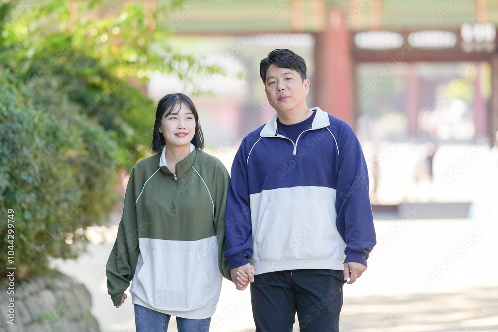 A Korean couple, a man in his 30s and a woman in her 20s, walks harmoniously through a historical building in Seoul, South Korea, wearing Hanbok. A Korean couple, a man in his 30s and a woman in her 20s, walks harmoniously through a historical building in Seoul, South Korea, wearing Hanbok.