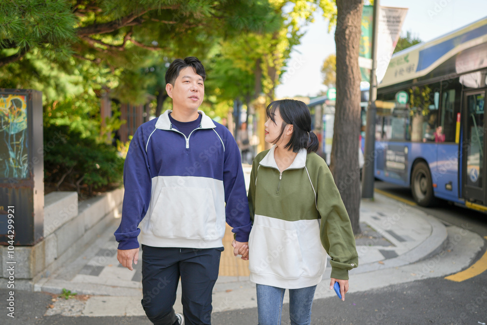 A couple, a Korean man in his 30s and a woman in her 20s, wearing tracksuits, enjoy an afternoon stroll on a public road in Seoul, South Korea. A couple, a Korean man in his 30s and a woman in her 20s, wearing tracksuits, enjoy an afternoon stroll on a public road in Seoul, South Korea.