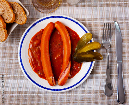 Two Viennese sausages with saftgoulash served with slices of pickled cucumbers. photo