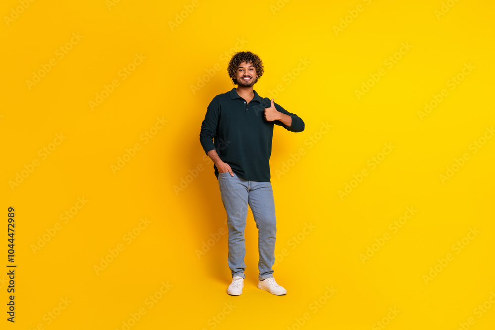 Young man wearing a black shirt and jeans gives a thumbs-up against a bright yellow background, showcasing a cheerful and positive attitude