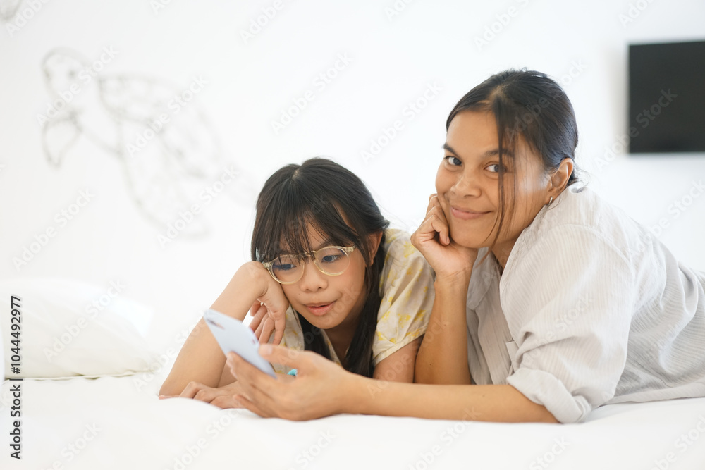 Close up caring Asian mother and little girl using smartphone together, lying on cozy bed in bedroom, family enjoying leisure time with gadget at home Close up caring Asian mother and little girl using smartphone together, lying on cozy bed in bedroom, family enjoying leisure time with gadget at home