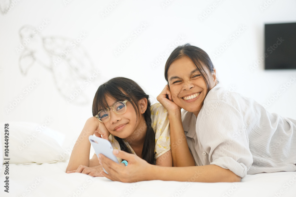 Close up caring Asian mother and little girl using smartphone together, lying on cozy bed in bedroom, family enjoying leisure time with gadget at home Close up caring Asian mother and little girl using smartphone together, lying on cozy bed in bedroom, family enjoying leisure time with gadget at home