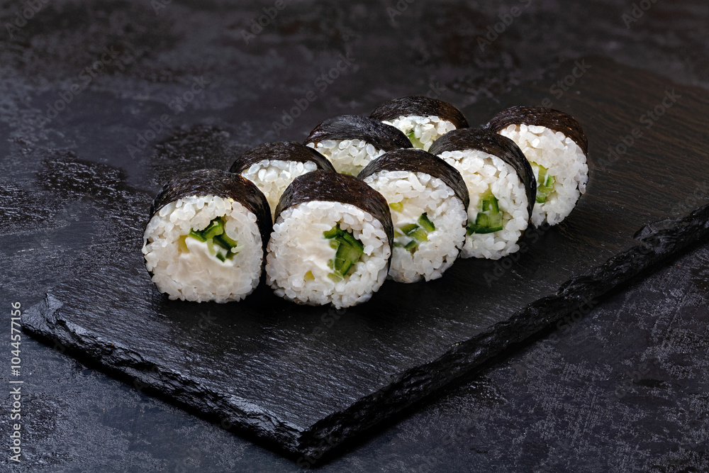 Japanese sushi rolls with cucumber and cream cheese in nori seaweed on black background Japanese sushi rolls with cucumber and cream cheese in nori seaweed on black background