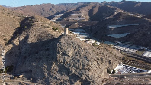 Aerial approach to the Cautor old watchtower in La Mamola, Granada, Spain. Greenhouses in the valley next to the sea. photo