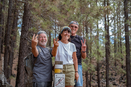 Happy group of senior friends enjoying vacation and adventure trekking in the forest, two elderly men and one woman looking at camera smiling. Sport, freedom, healthy lifestyle concept #1044612369