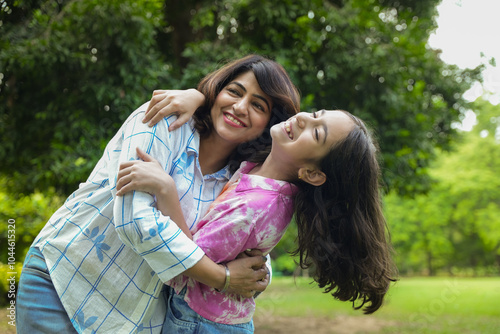 Young palyful indian mom and kid daughter having fun together at summer park, hugging and laughing. bonding, Togetherness, Mental health. photo