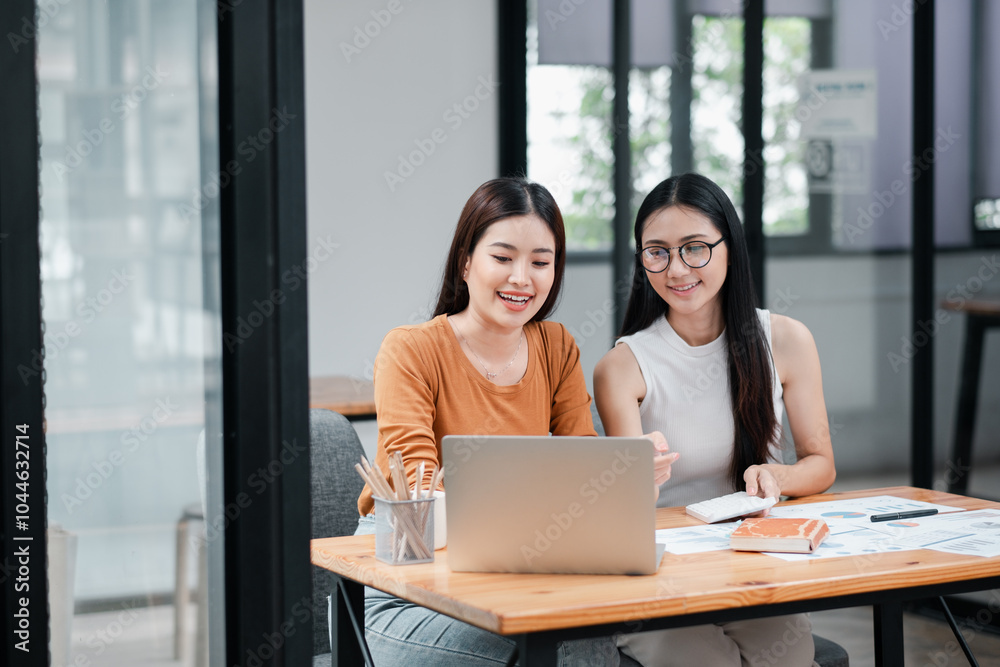 Two young women working together in a modern office, discussing ideas with a laptop and documents on the table. Two young women working together in a modern office, discussing ideas with a laptop and documents on the table.