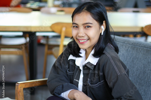 excited asian woman sitting in cafe and smiling at camera with confidence wearing earphone, cloes up photo