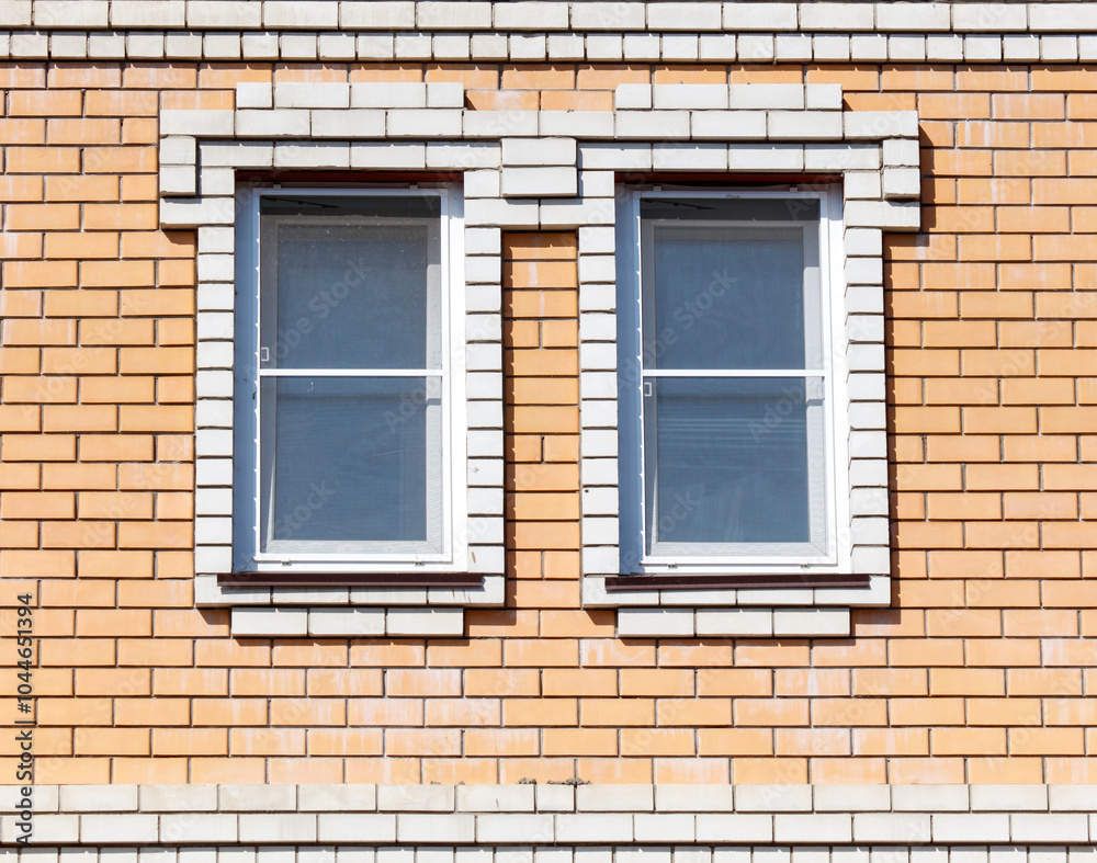 Two windows with white frames sit on a brick wall Two windows with white frames sit on a brick wall