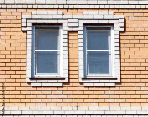 Two windows with white frames sit on a brick wall