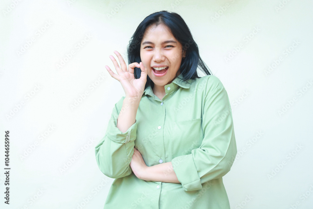 delighted asian woman with dark hair wearing green over size clothes showing ok signs with folding arms looking at camera screaming satisfied isolated on white background delighted asian woman with dark hair wearing green over size clothes showing ok signs with folding arms looking at camera screaming satisfied isolated on white background