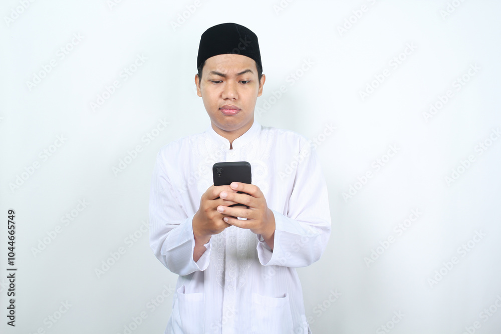 serious muslim asian man watching mobile phone with confused expression isolated on white background serious muslim asian man watching mobile phone with confused expression isolated on white background