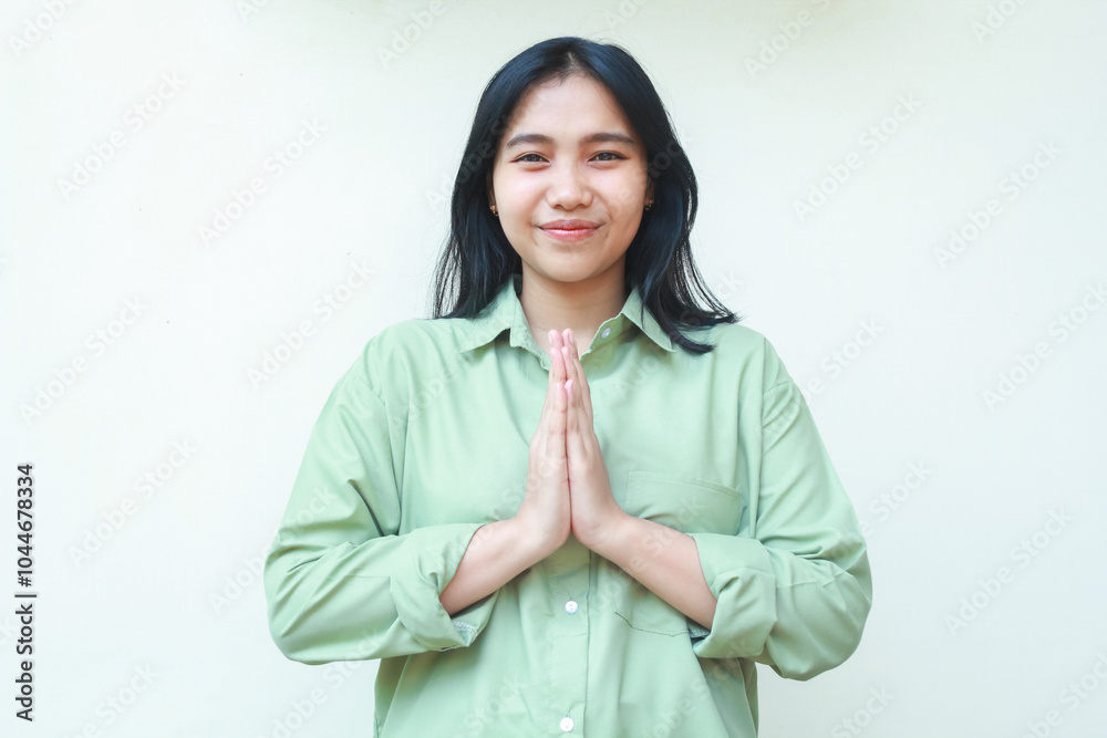 happy asian woman wearing green oversized shirt looking at camera gesturing traditional greeting and smiling with pleasure, feeling pleased, standing over isolated background happy asian woman wearing green oversized shirt looking at camera gesturing traditional greeting and smiling with pleasure, feeling pleased, standing over isolated background