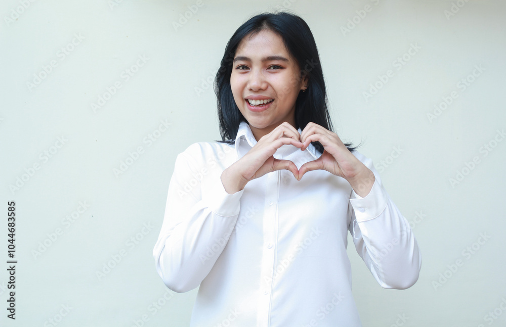 success confident asian young business woman making heart shape over chest as love signs, looking at camera feeling pleased, wearing white formal suit shirt, standing over isolated background
